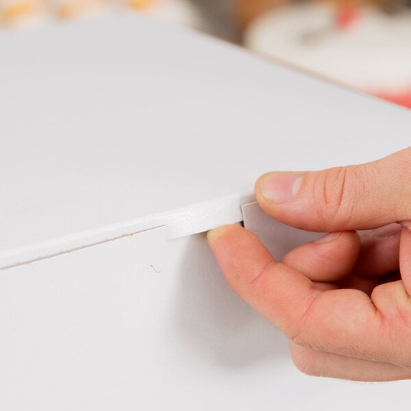 A hand closing the tab of a white cardboard bakery box.