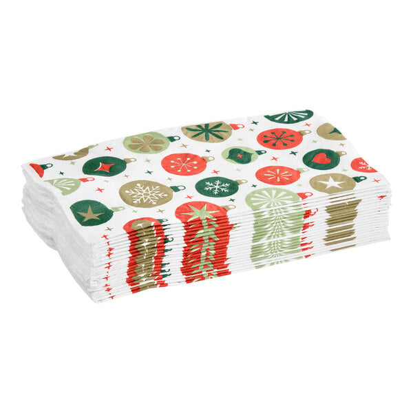 A stack of white napkins featuring a festive ornament print in red, green, and gold colors.
