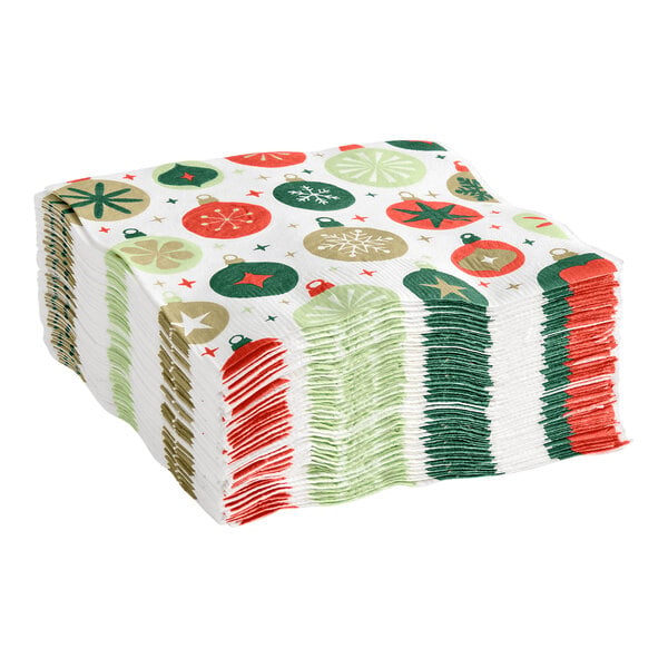 A stack of white napkins featuring a festive ornament print in red, green, and gold colors.