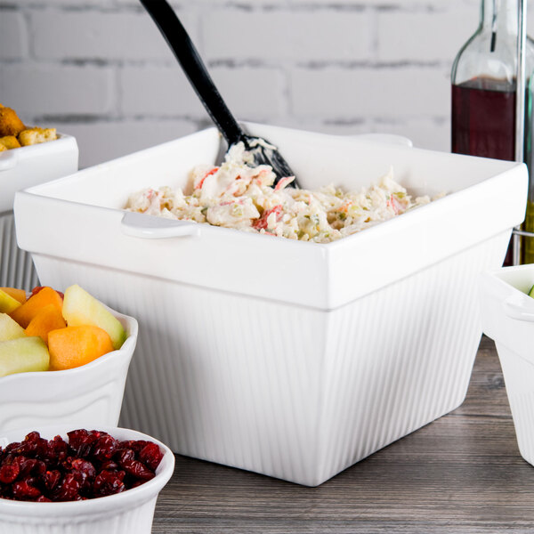 A Tablecraft white cast aluminum bowl filled with salad next to a bowl of fruit.