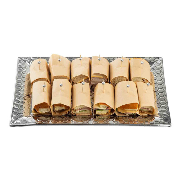 A large rectangular stainless steel serving tray with a honeycomb pattern, holding several wrapped sandwich halves secured with toothpicks.