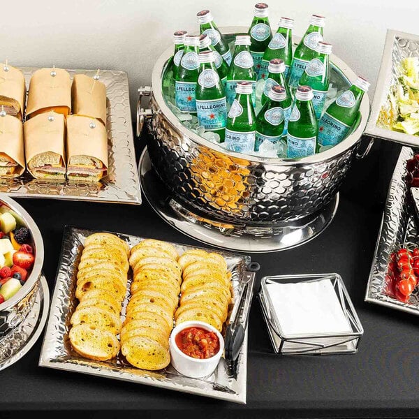 A round, double-walled stainless steel beverage tub with a hammered honeycomb design, filled with bottled drinks and ice.