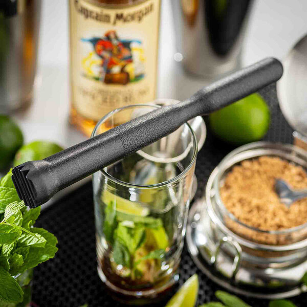 A black ABS plastic muddler resting on a glass with cocktail ingredients.
