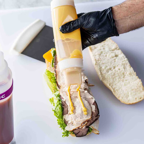 A dual-tip squeeze bottle being used to dispense sauce onto a sandwich.