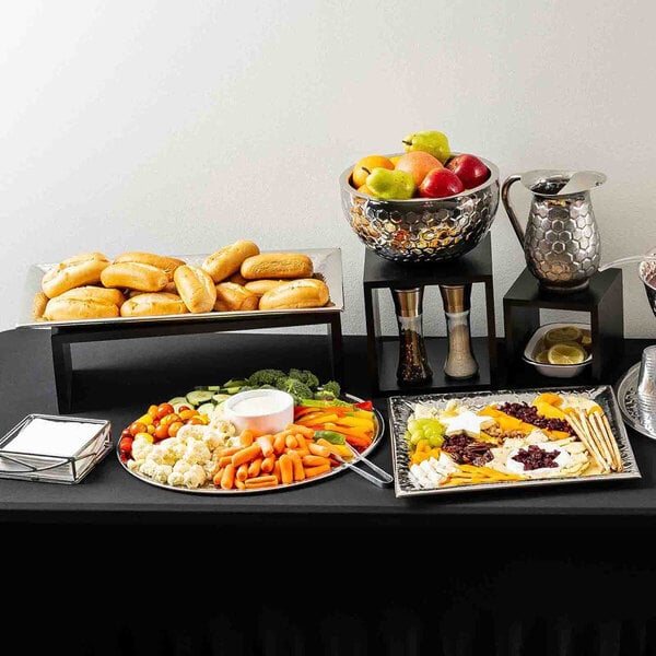 An 18-inch round stainless steel serving tray with a honeycomb pattern, displayed as part of a buffet setup with vegetables and dip.