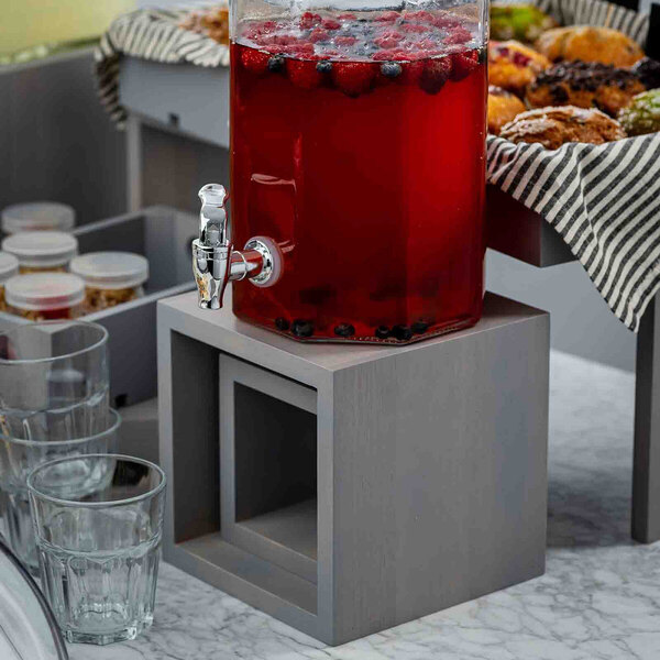 A three-piece square gray wood riser set used to elevate and display food and beverage dispensers.