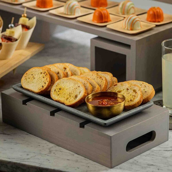 A gray wood serving and display crate holding a platter of sliced bread and a bowl of dip.