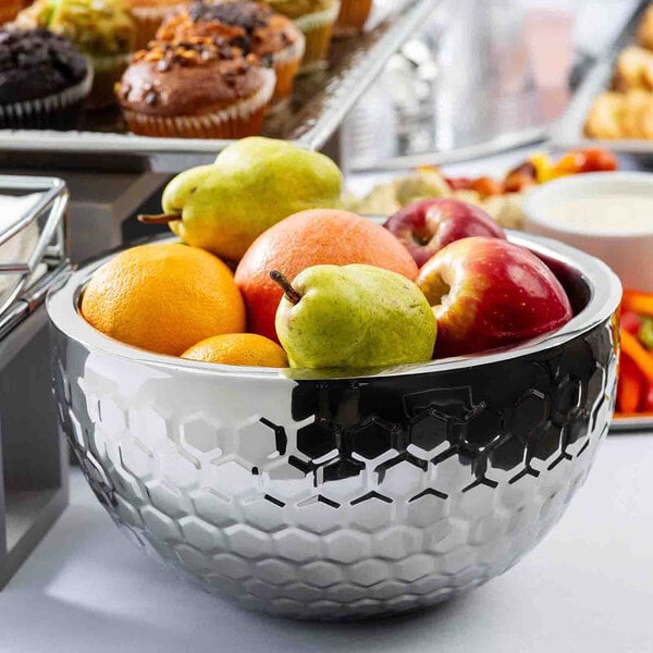 A round, double-walled stainless steel serving bowl with a honeycomb pattern, filled with assorted fruits.