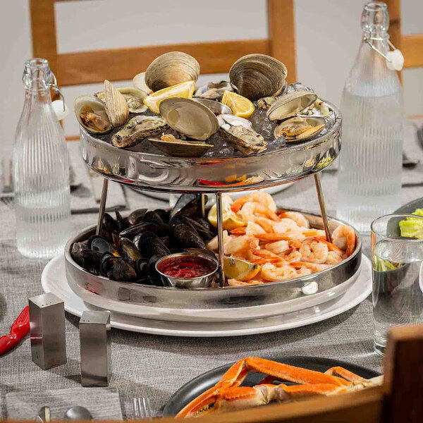 A two-tier stainless steel seafood tower filled with assorted shellfish and served on a dining table.