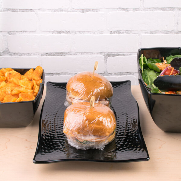 A black Carlisle rectangular scalloped platter with sandwiches and vegetables on it.