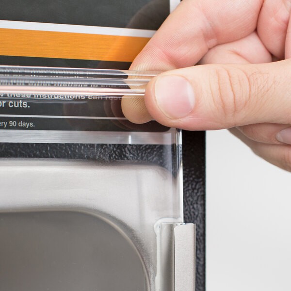 A person holding a Hamilton Beach plastic splash shield over a plastic container on a counter.