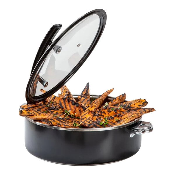 A round black steel buffet server with a glass lid, containing grilled food arranged in a circular pattern.