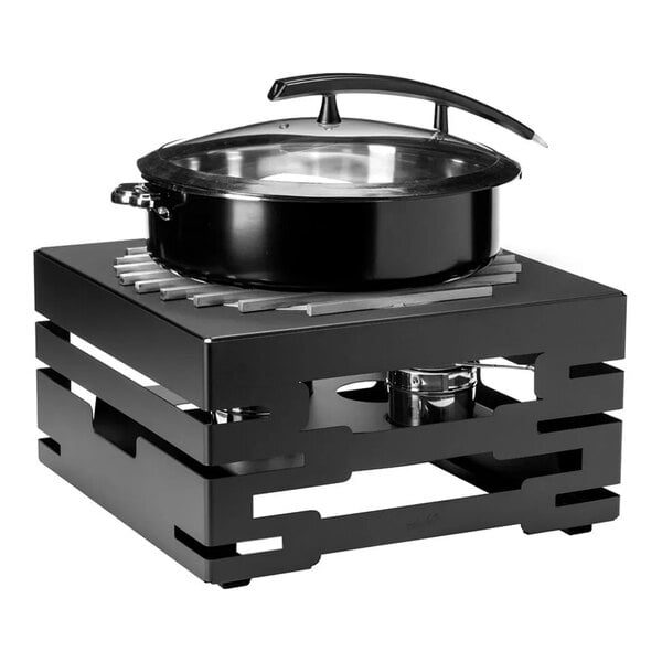 A black round pot with a glass lid sits on a modern, square, black metal buffet server with a visible fuel holder underneath.