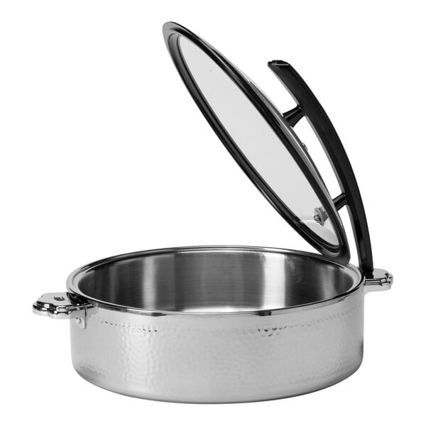 A round, hammered steel buffet server with a glass lid that is propped open, featuring side handles.