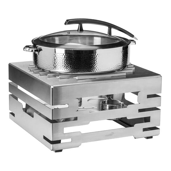 A square, modern stainless steel buffet server with a hammered steel round pot and a glass lid, featuring a geometric base and a fuel holder underneath.