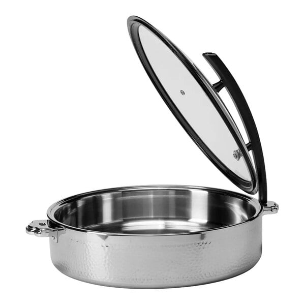 A round, hammered steel buffet server with a glass lid that is propped open, featuring side handles and a shiny metallic finish.