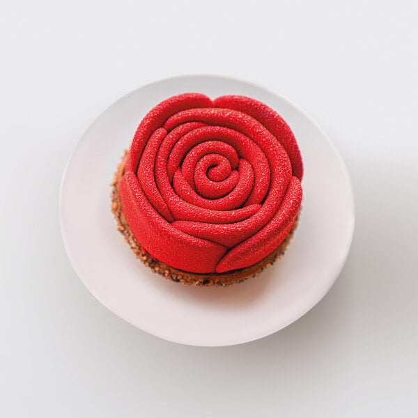 A dessert shaped like a red rose with a textured surface, presented on a white plate.