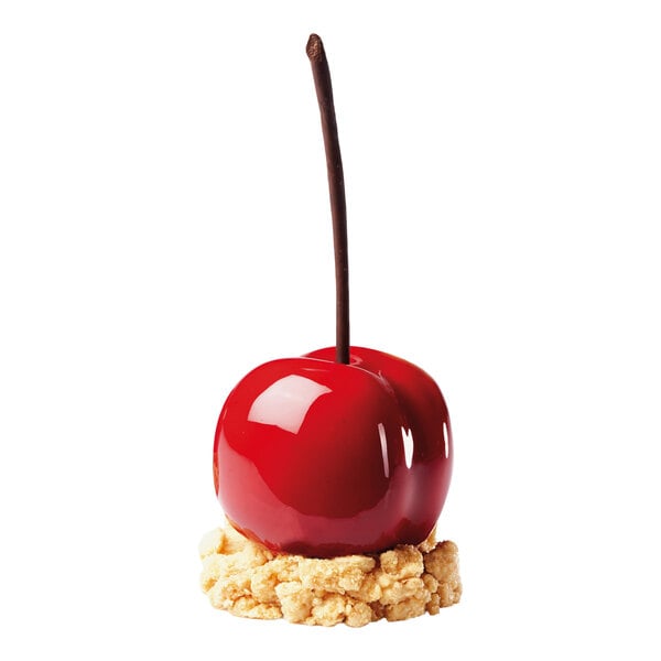 A glossy, cherry-shaped dessert with a long stem sits on a crumbly base against a white background.