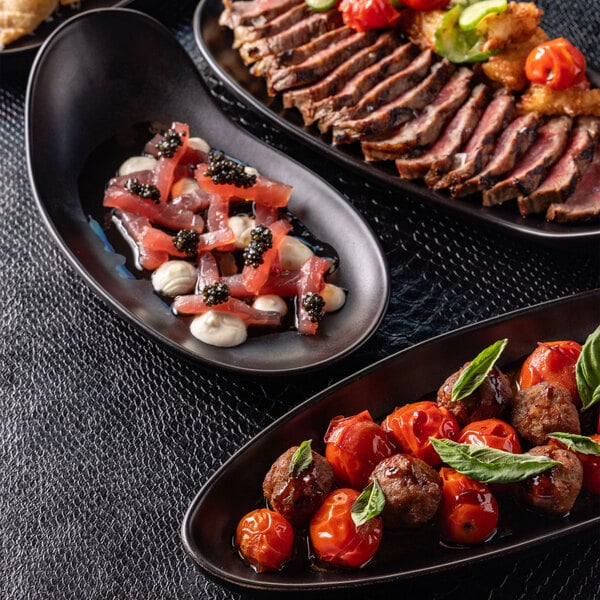 A matte black, oval-shaped stoneware tray with a handle, shown holding a gourmet appetizer.