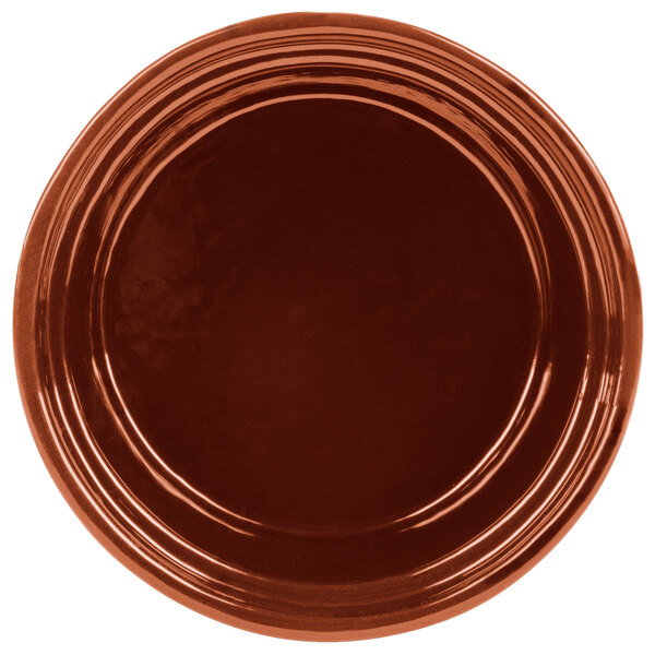 A copper cast aluminum souffle bowl with ridges on a brown plate.