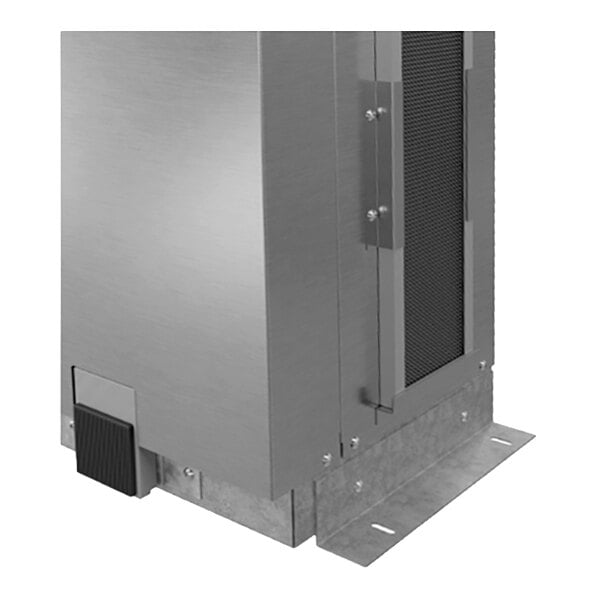 A close-up view of a metallic, rectangular structure with a vented panel and a foot pedal at the base, mounted on a flat metal plate.