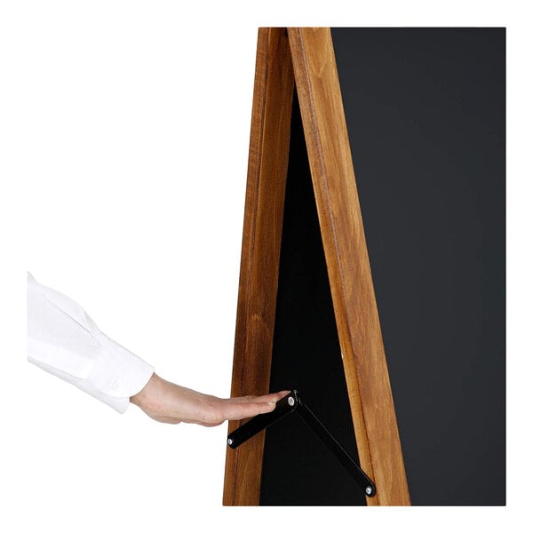 A person is adjusting the support bar of a wooden A-frame chalkboard.