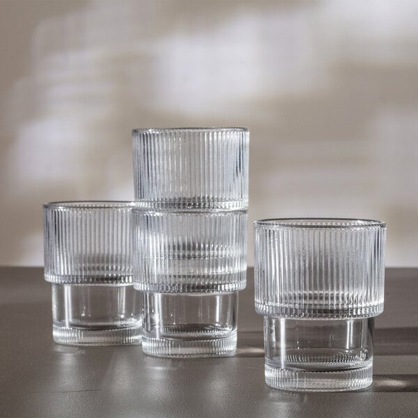 Four clear, stackable glasses with vertical ribbed patterns are arranged on a flat surface.