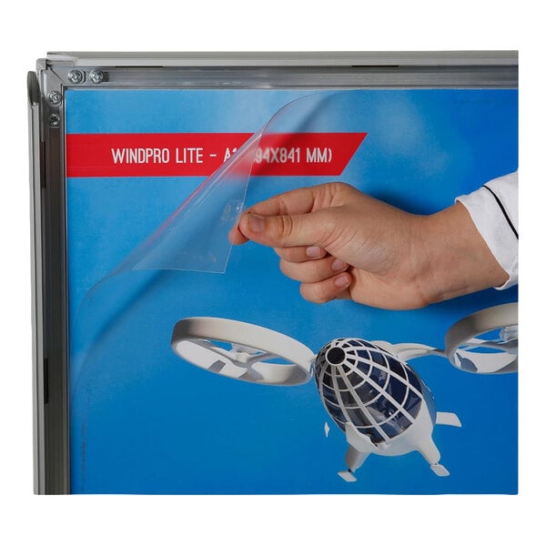 A hand is lifting a clear protective cover from a framed sign displaying a blue background with text and a graphic.