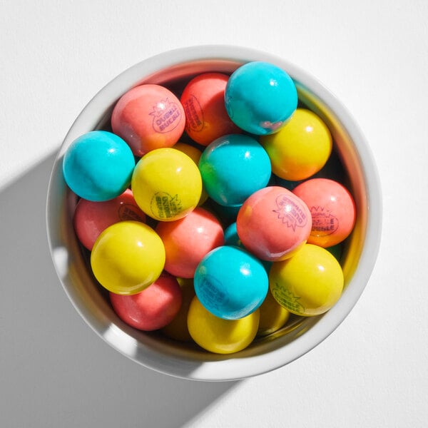 A bowl filled with colorful round gumballs in blue, yellow, and pink hues.