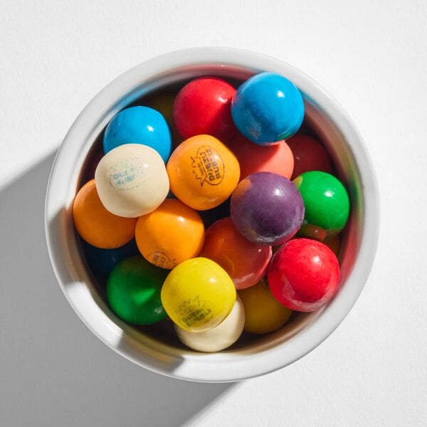 A white bowl filled with colorful, round gumballs in various shades including blue, red, yellow, green, orange, purple, and white.
