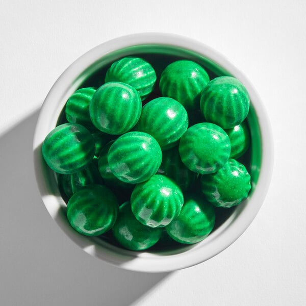 A white bowl filled with shiny, green, round gumballs that have a striped pattern resembling watermelons.