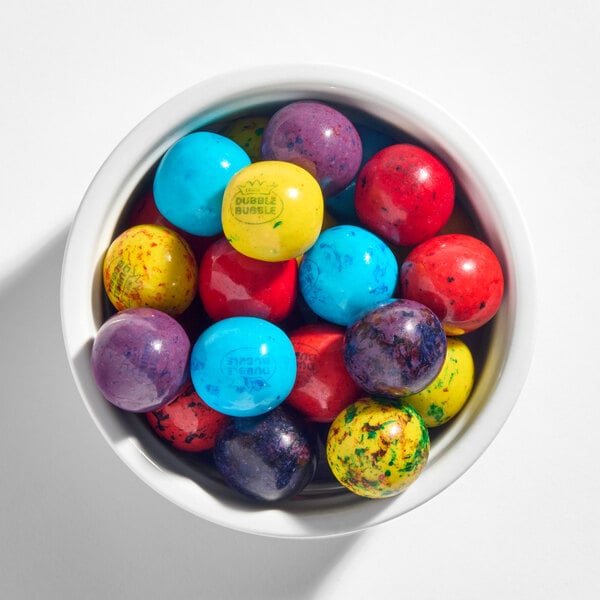 A white bowl filled with colorful, round gumballs in blue, yellow, red, and purple hues.