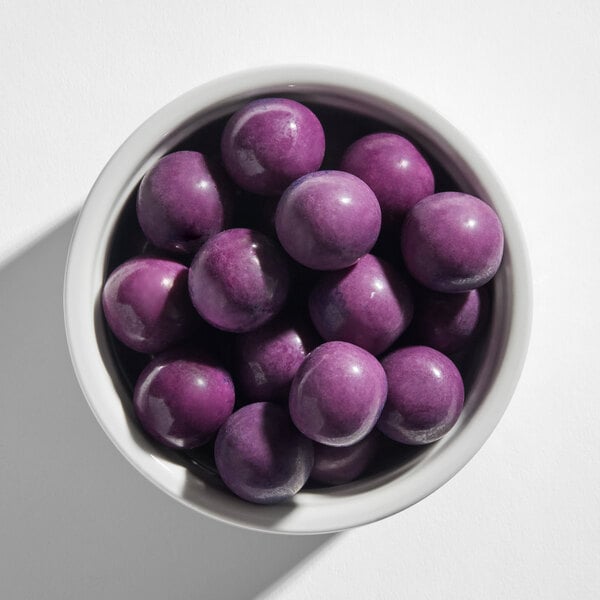 A white bowl filled with shiny, round, purple gumballs.