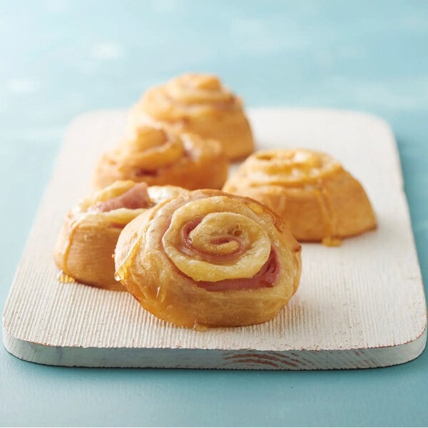 Four golden-brown pastry rolls are arranged on a white wooden board against a light blue background.