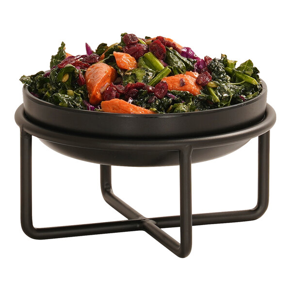 A black round bowl filled with a colorful salad, placed on a modern black metal wire stand.
