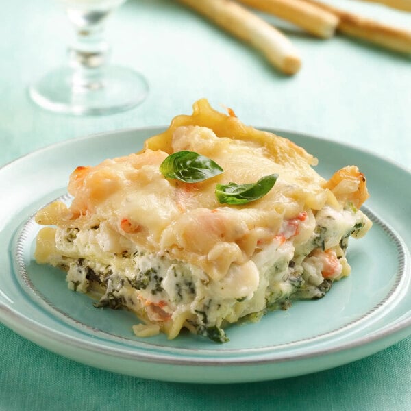 A slice of creamy, layered lasagna garnished with fresh basil leaves on a light blue plate.