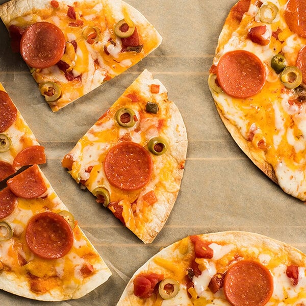 Several slices of pizza with pepperoni, cheese, and green olives are arranged on a sheet of parchment paper.