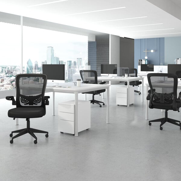 A modern office space with several black mesh ergonomic chairs, white desks, and computer monitors, set against large windows with a city view.