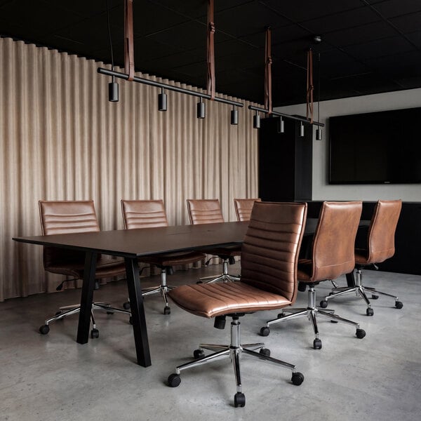 A modern conference room with brown armless office chairs on wheels around a dark rectangular table, set against a backdrop of beige curtains and a wall-mounted screen.