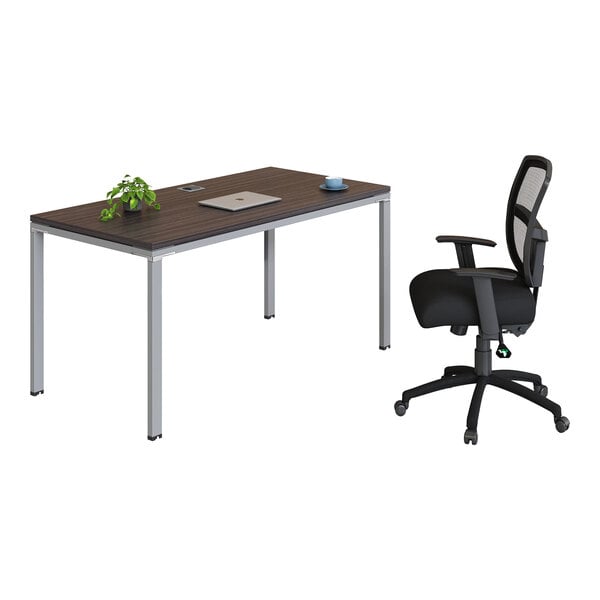 A modern office setup featuring a rectangular desk with a dark wood-like surface, a small plant, a closed laptop, a cup, and a black ergonomic office chair with a mesh back.