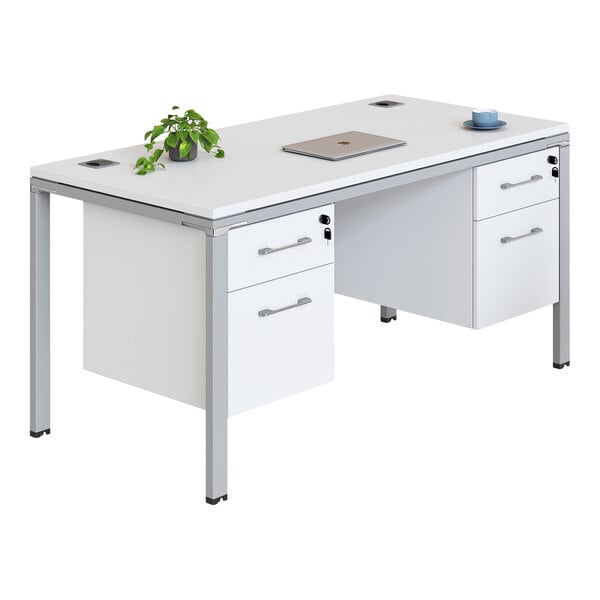 A modern white office desk with metal legs, featuring drawers on both sides, a potted plant, a closed laptop, and a cup with a saucer on top.
