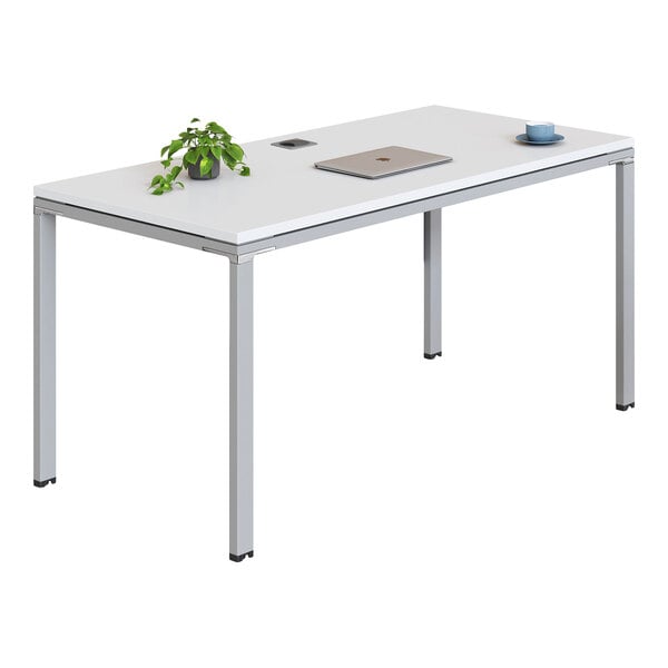 A modern rectangular desk with a white tabletop, metal legs, a small potted plant, a closed laptop, and a cup with a saucer on top.