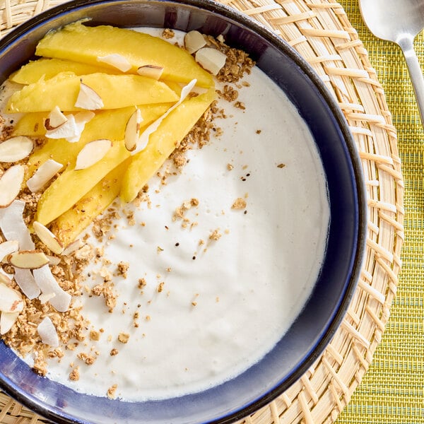 A bowl of creamy white sorbet topped with sliced mango, granola, coconut flakes, and almond slivers.