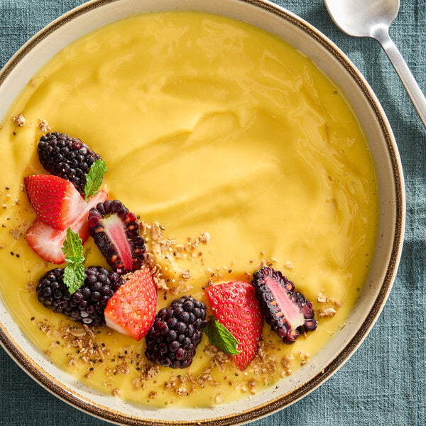 A bowl of smooth yellow mango sorbet topped with fresh strawberries, blackberries, granola, and mint leaves.