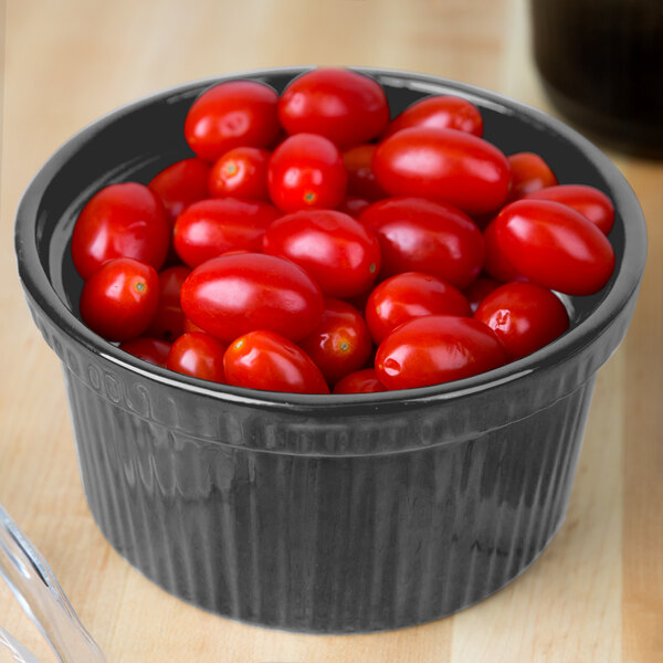 A Tablecraft natural cast aluminum souffle bowl filled with cherry tomatoes on a counter.