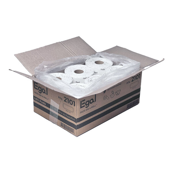 An open cardboard box containing several rolls of white pads, each individually wrapped in plastic.