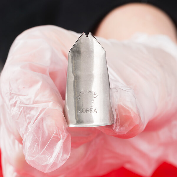 A person wearing a clear glove is holding a metal piping tip with a V-shaped opening.
