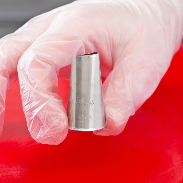 A gloved hand is holding a stainless steel piping tip with a curved, angled opening.