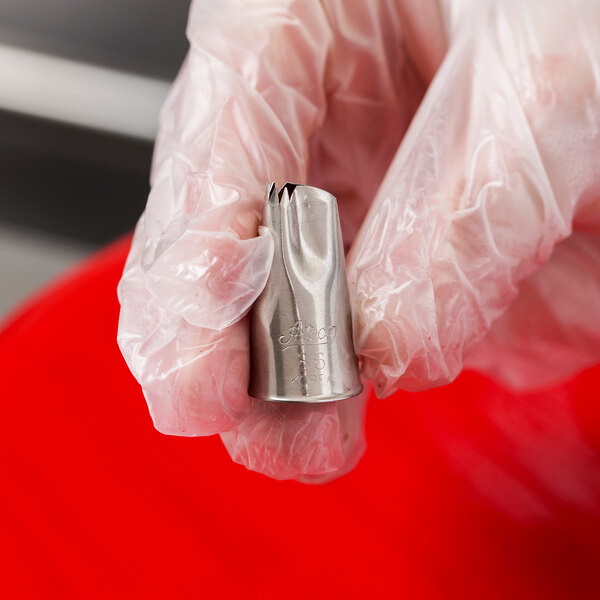 A gloved hand is holding a metal piping tip with a ruffled opening.