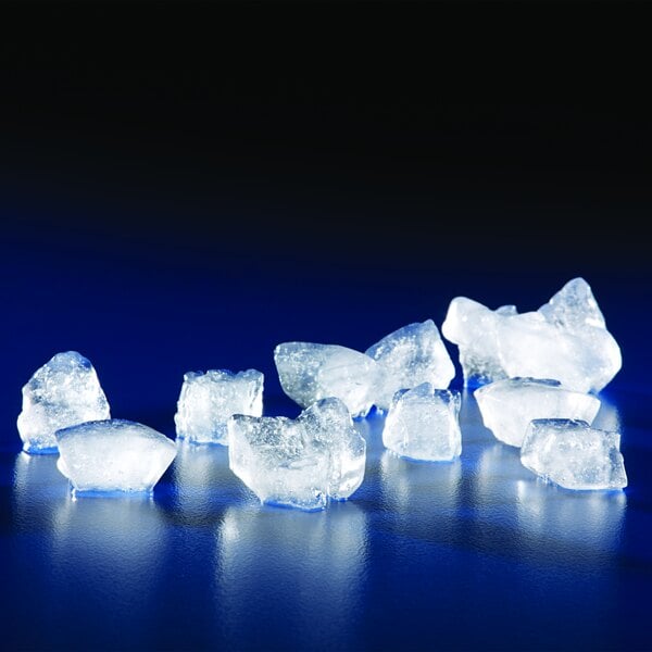 Several irregularly shaped, translucent ice nuggets are scattered on a reflective blue surface with a dark background.